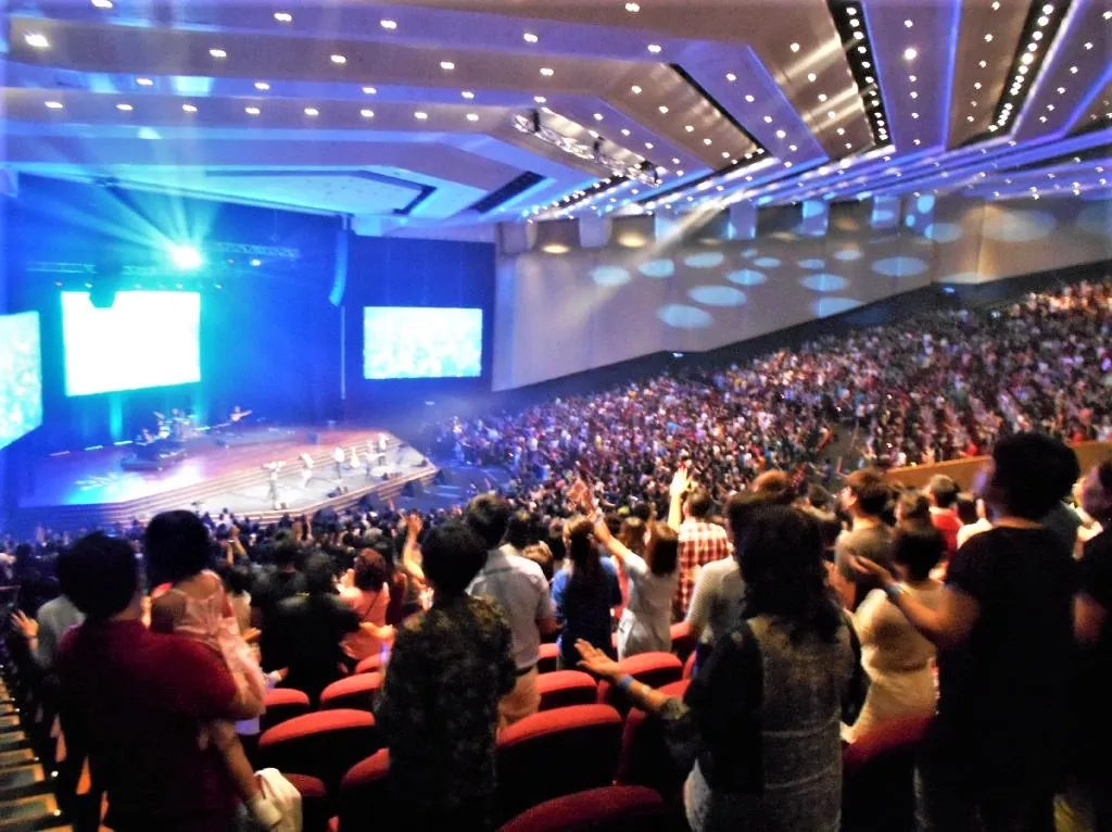 Audience standing and raising their hands in the Auditorium, facing the stage and screens