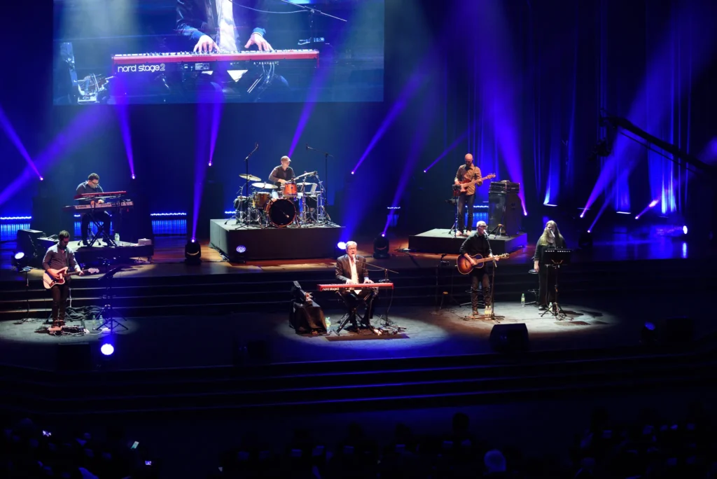 Band playing on the Auditorium stage under blue spotlights, with a keyboard close-up on the screen above