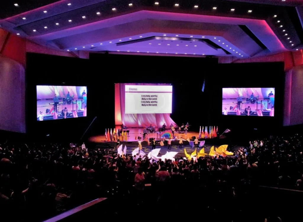 Conference session in the Auditorium, with the stage and three screens lit in pink