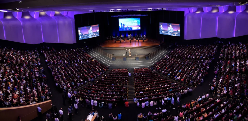 Full Auditorium seen from the upper seats, with the stage and three screens at the front