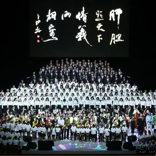 Large choir on tiered risers under a Chinese calligraphy backdrop in the Auditorium