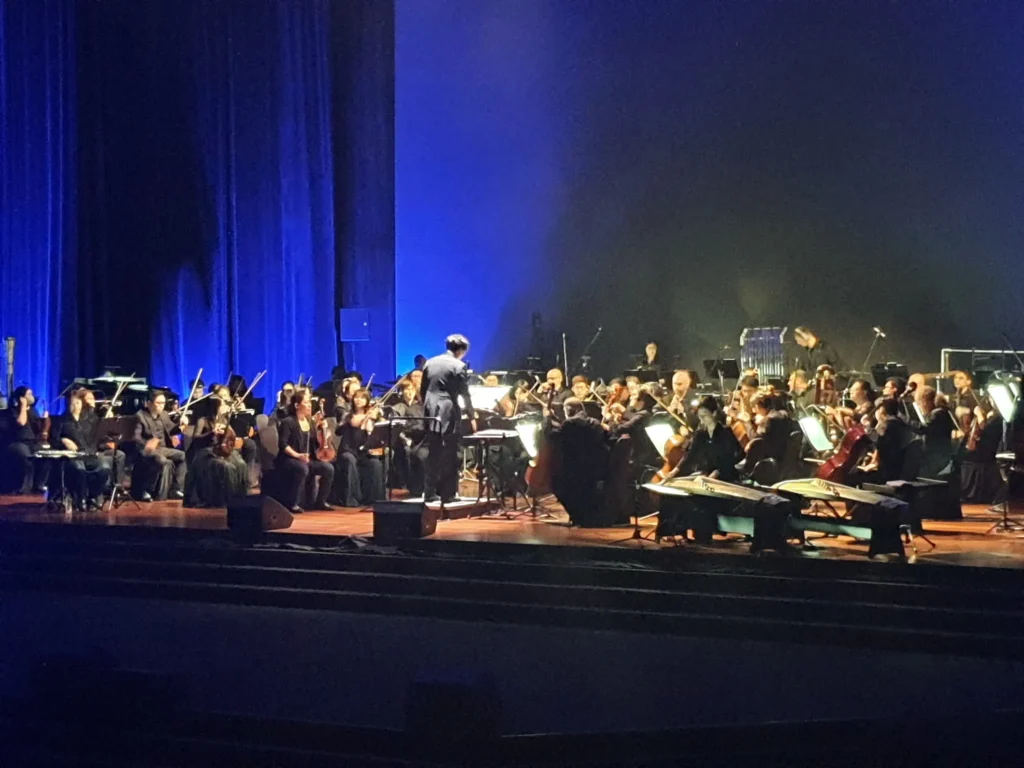 Orchestra and conductor on the Auditorium stage in front of a blue curtain