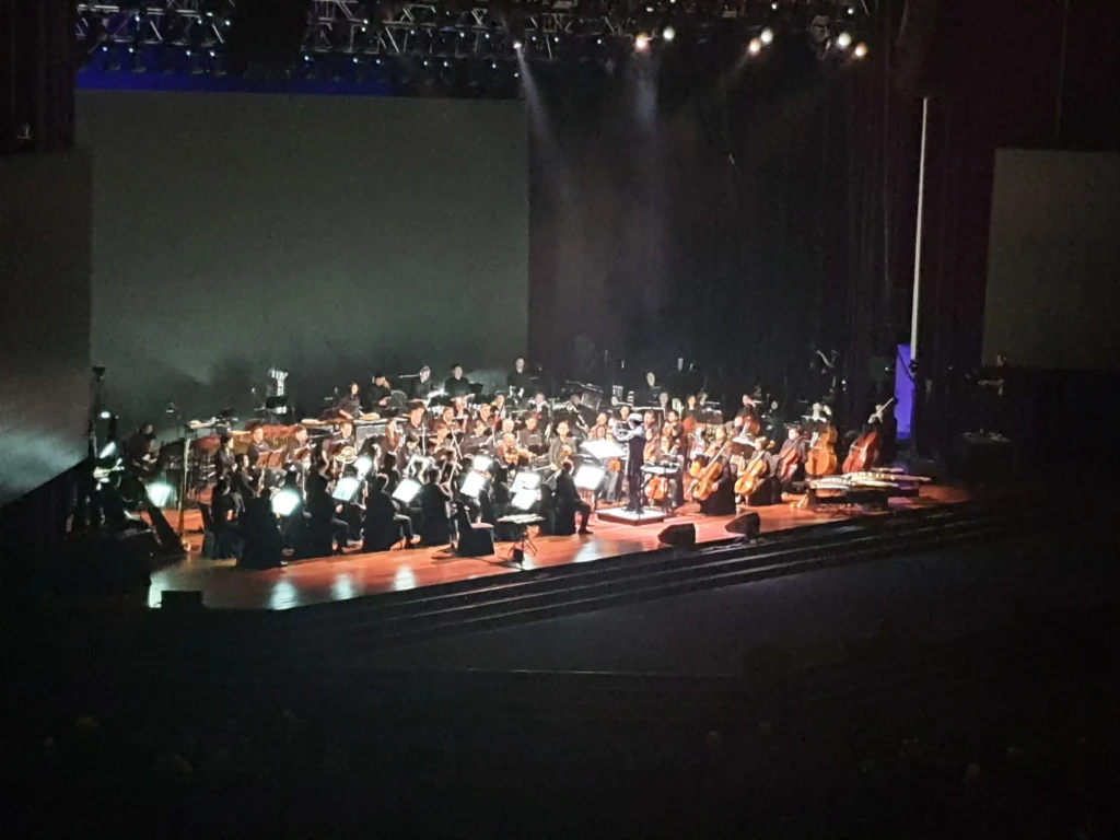 Orchestra performing under spotlights on a darkened Auditorium stage