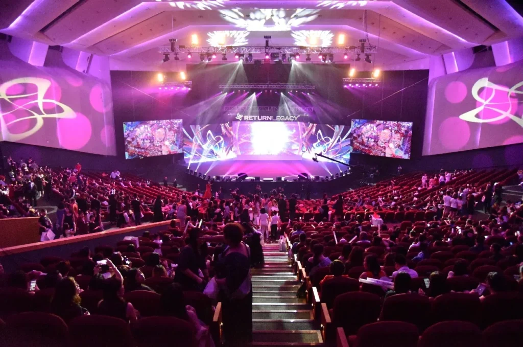Full Auditorium audience facing a lit stage and LED screens at a Return Legacy event