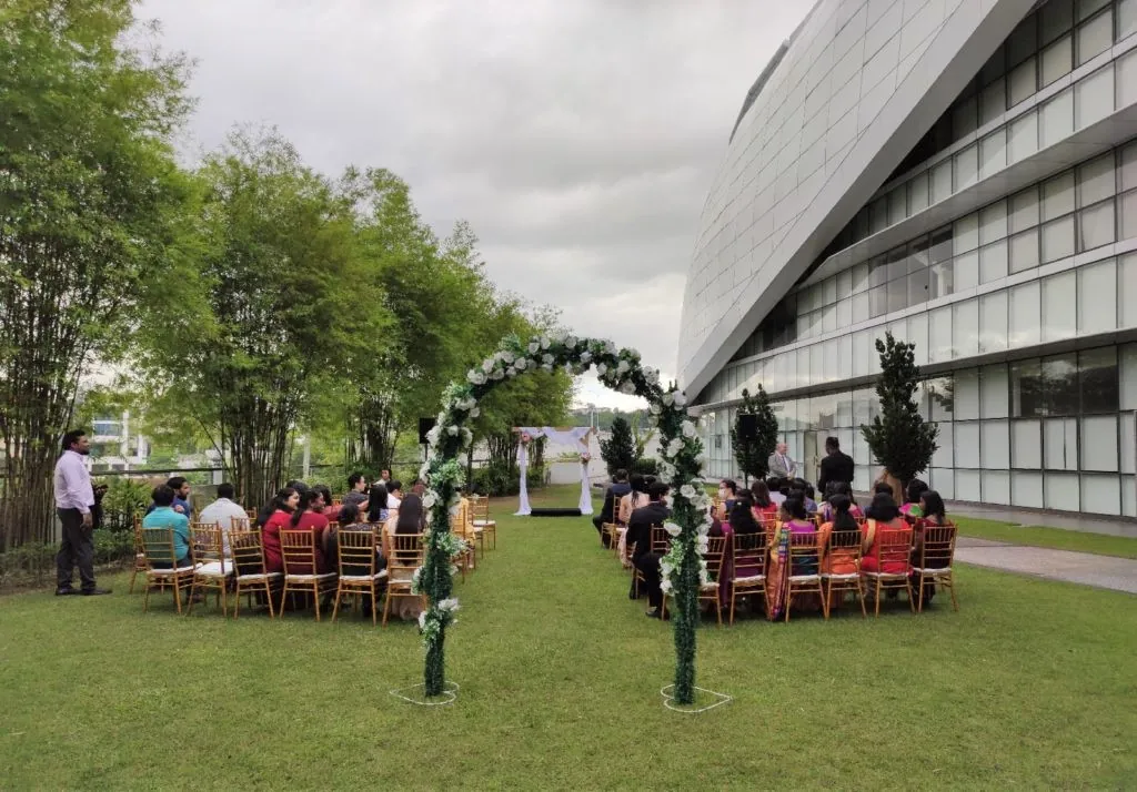 Wedding guests seated behind a floral arch on the Garden lawn beside the building