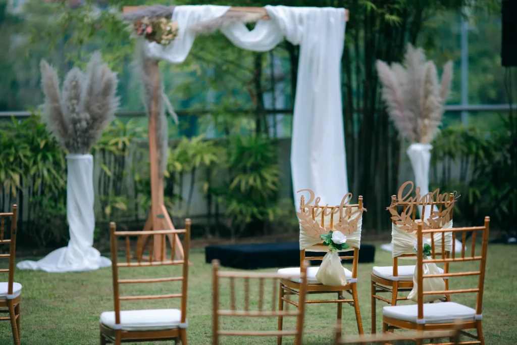Wedding arch with white drapes and pampas grass behind gold chairs in the Garden