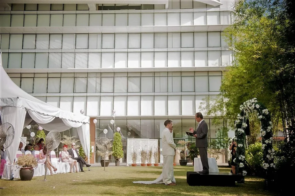 Wedding ceremony on the Garden lawn beside a white tent and a floral arch