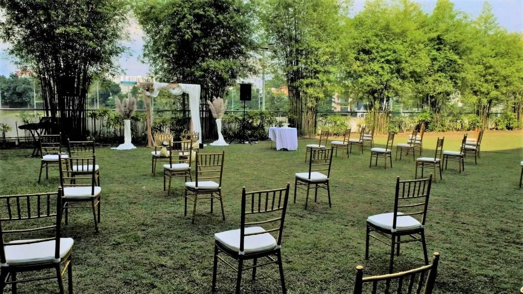 Spaced-out gold chairs on the Garden lawn facing a wedding arch, with bamboo behind