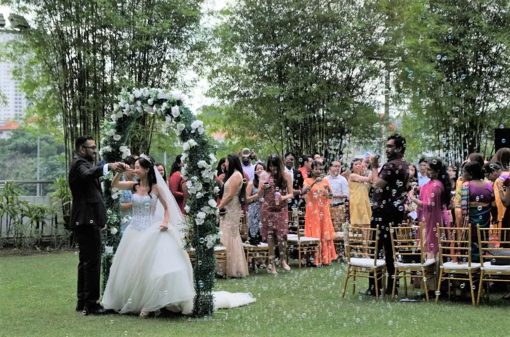 Bride and groom under a floral arch as guests throw confetti in the Garden