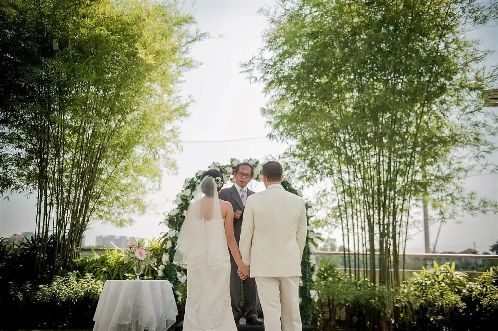 Bride and groom facing the officiant under an arch framed by bamboo in the Garden
