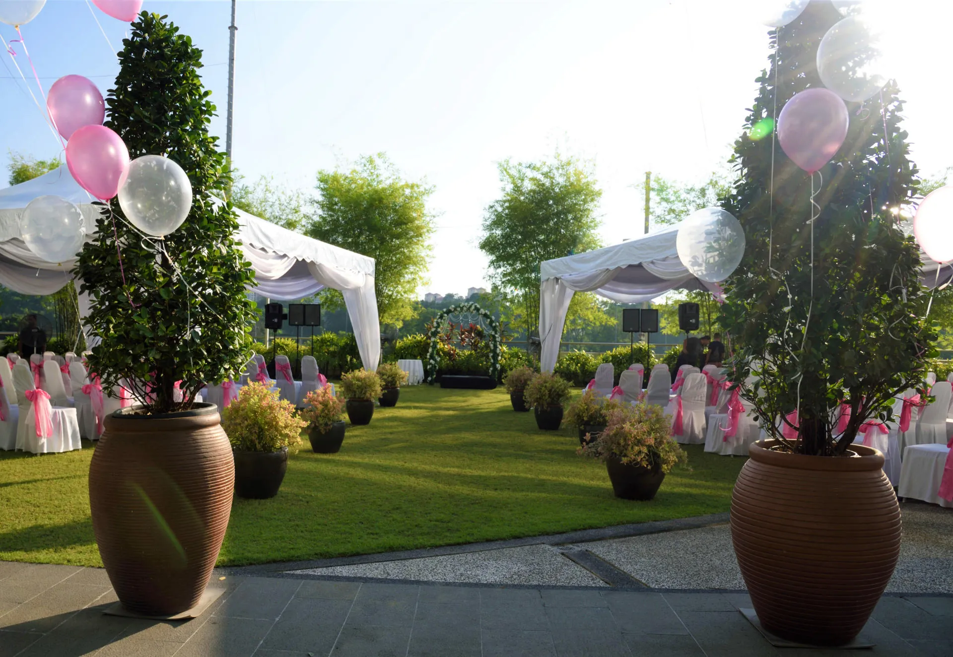 Garden wedding setup with white tents, potted topiaries and pink balloons on the lawn