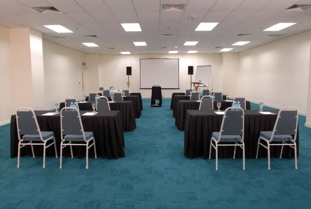 Classroom-style tables with black cloths and grey chairs facing a screen in a meeting room