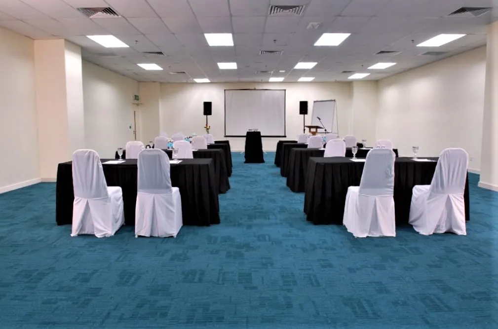 Rows of tables with white-covered chairs facing a projector screen in a meeting room