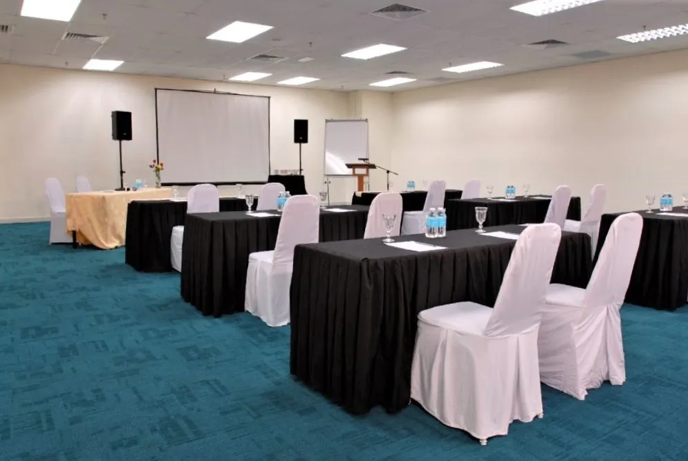 Classroom-style tables with white chair covers facing a screen and lectern in a meeting room
