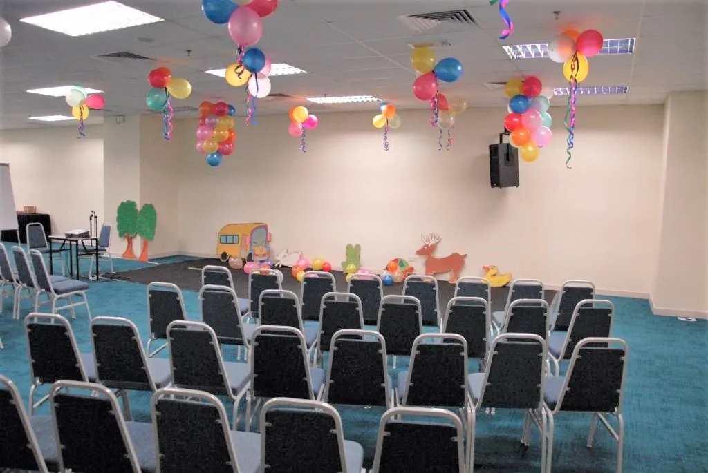 Meeting room set up for a kindergarten show, with cut-out scenery and balloon decorations