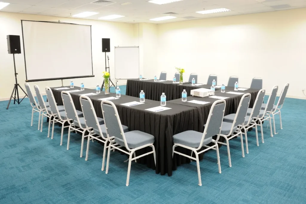 Black-draped tables in a U-shape open towards the projector screen in a meeting room