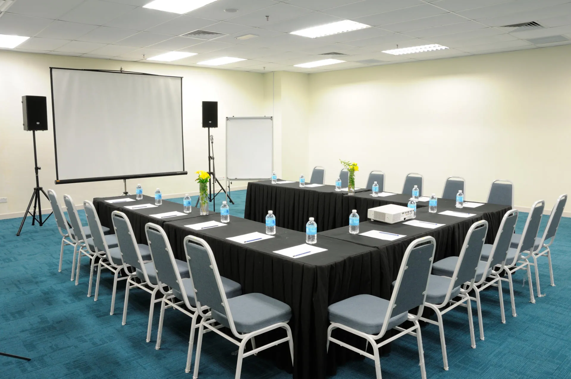 Meeting room with tables in a U-shape facing a projector screen