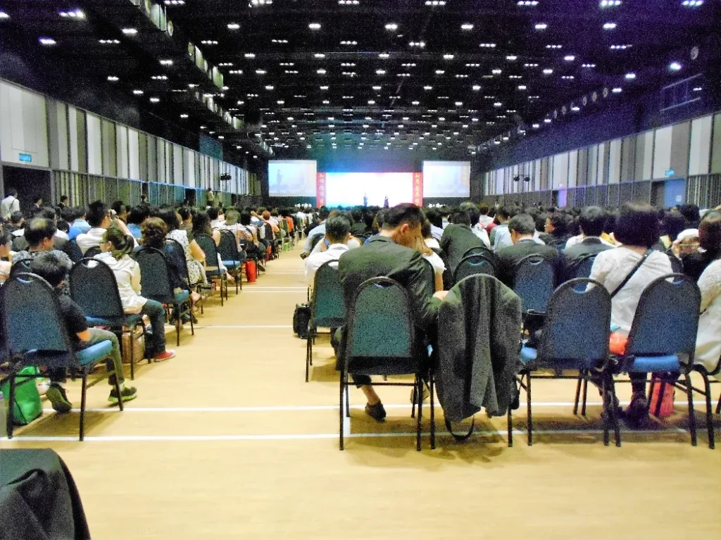 Audience seen from the back, facing the stage screens in the Multipurpose Banquet Hall