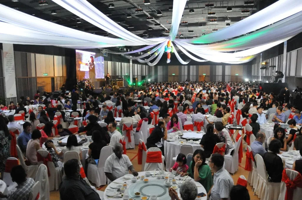 Dinner gala under white ceiling drapes, with a speaker on the stage screen, in the Multipurpose Banquet Hall