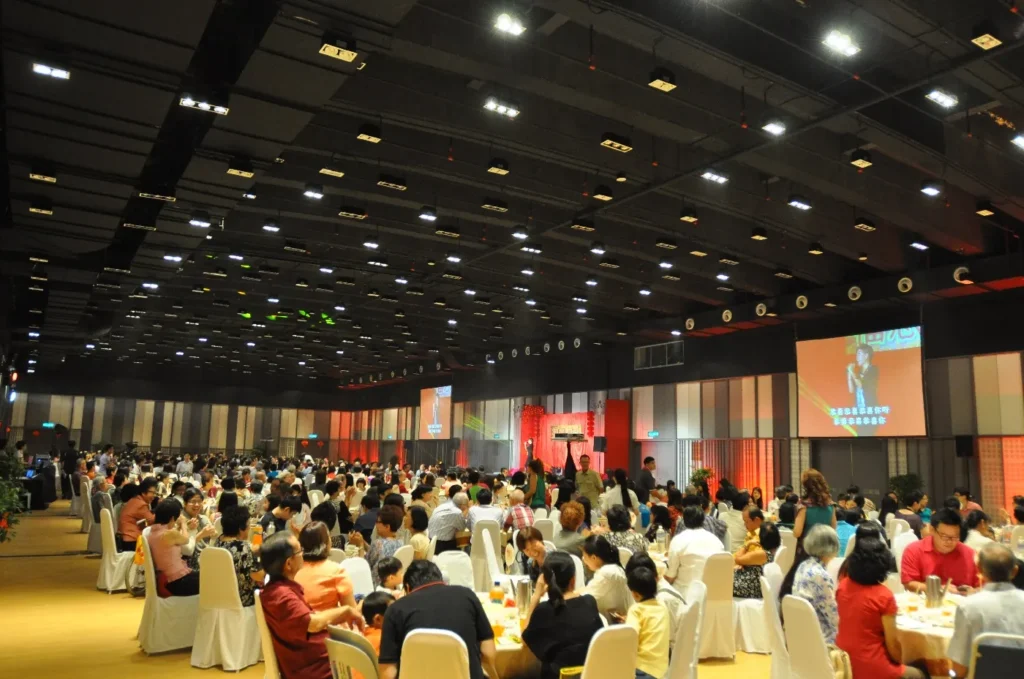 Full hall of dinner guests watching a performer on screen at a gala in the Multipurpose Banquet Hall