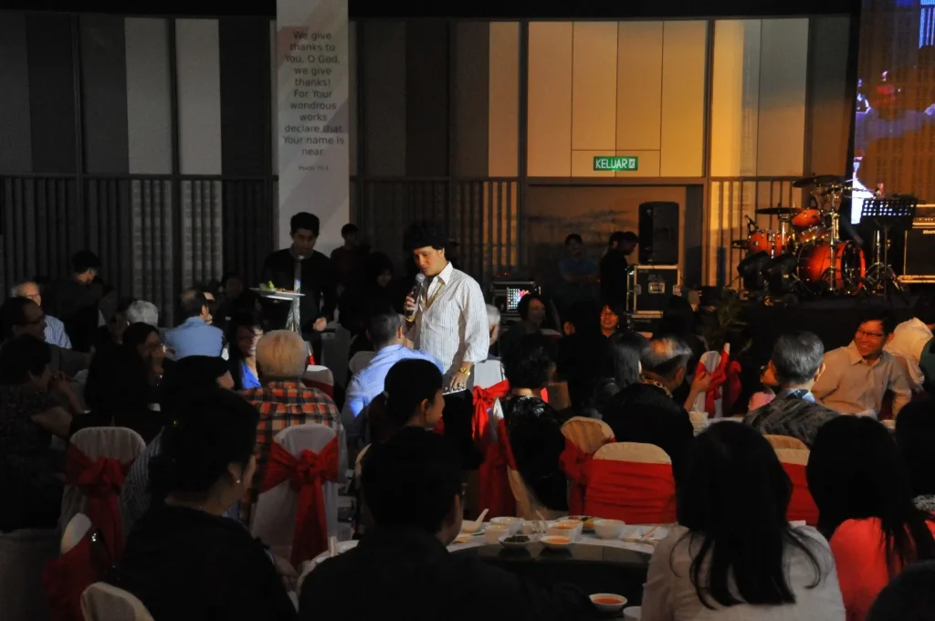 Guest speaking into a microphone among dinner tables at a gala in the Multipurpose Banquet Hall