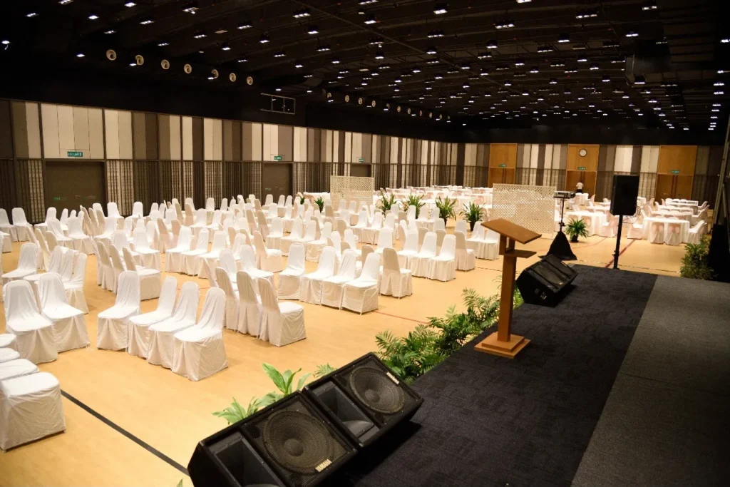 Lectern and loudspeakers on the stage, facing rows of white-covered chairs in the Multipurpose Banquet Hall