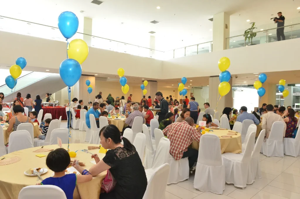 Guests eating at round tables decorated with blue and yellow balloons in the Multipurpose Banquet Hall lobby
