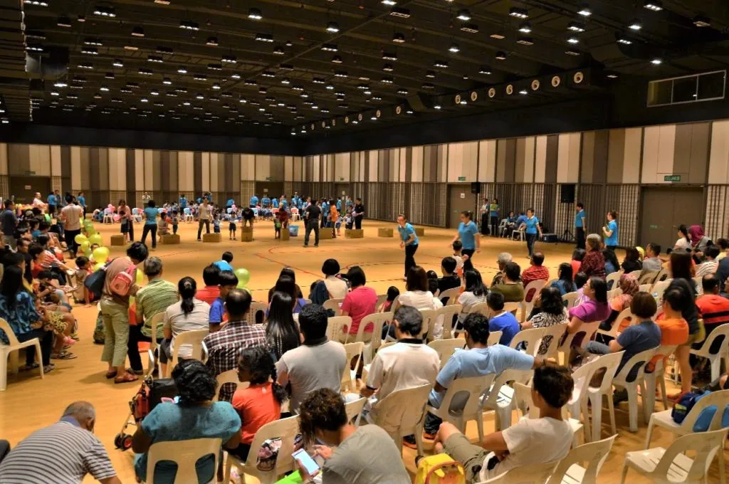 Families seated in plastic chairs at a kindergarten sports day in the Multipurpose Banquet Hall
