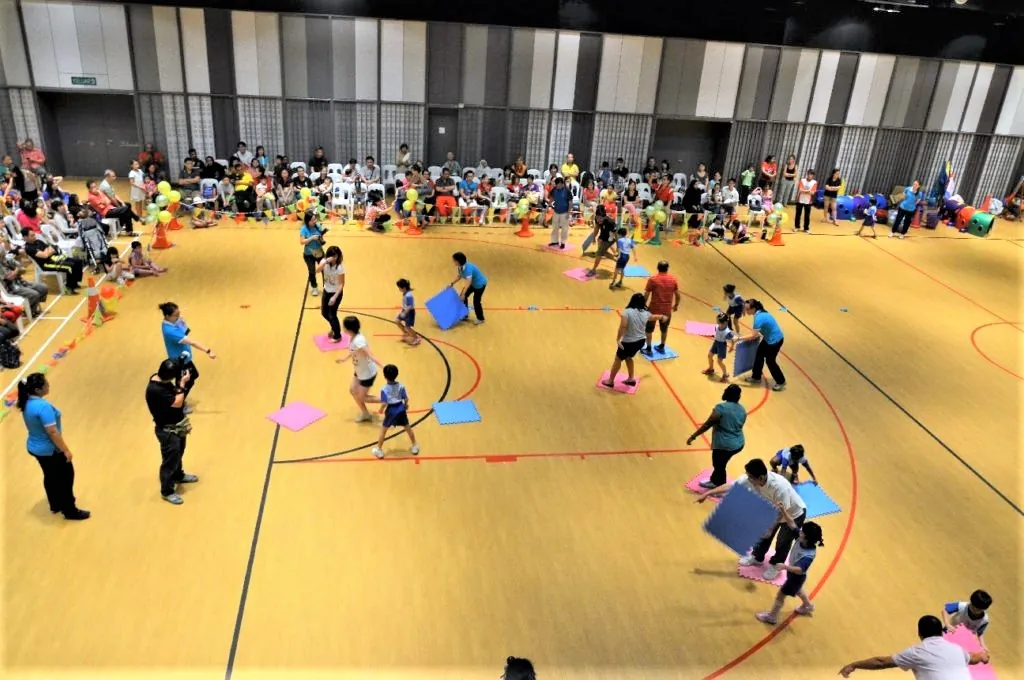Children and parents playing games with coloured mats at a kindergarten sports day in the Multipurpose Banquet Hall