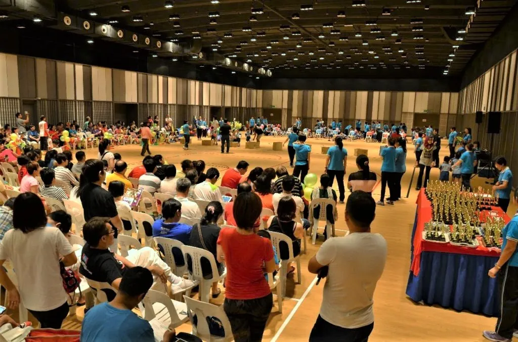Families watching a kindergarten sports day, with a table of trophies at the front of the Multipurpose Banquet Hall