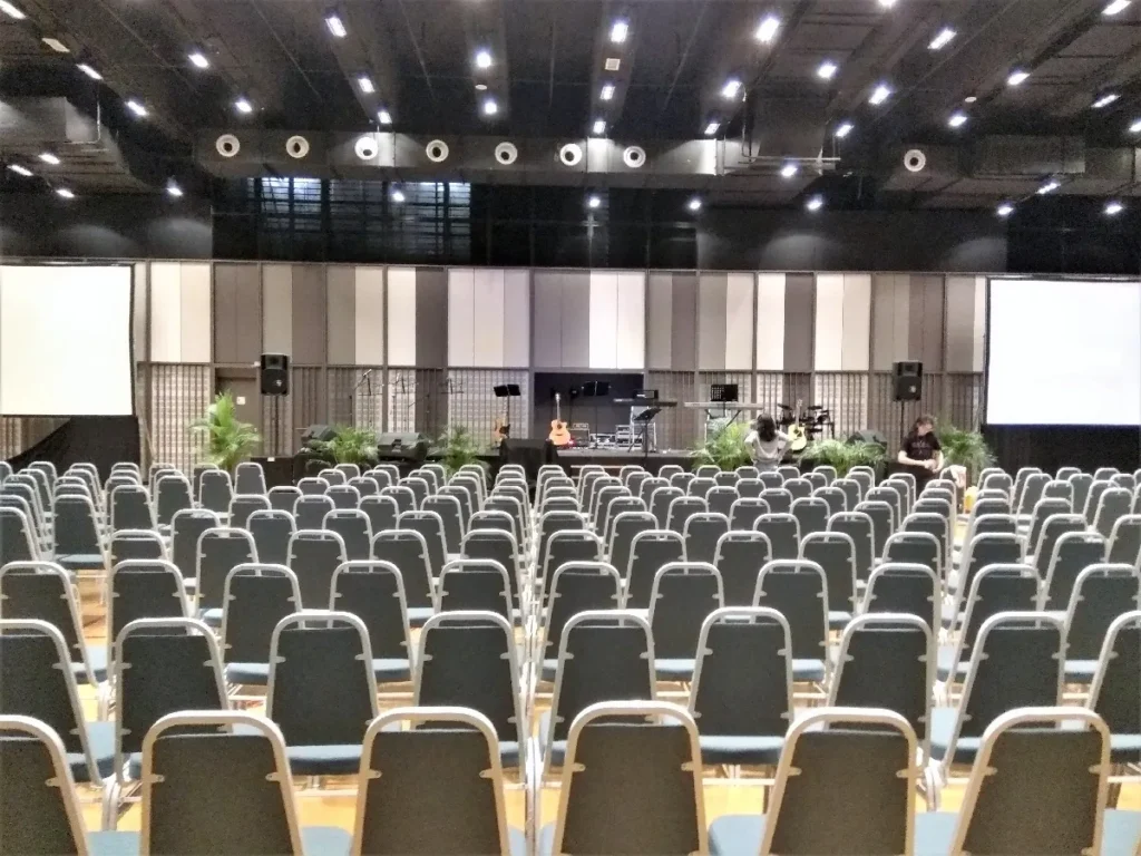 Rows of chairs facing a stage with band equipment and two screens in the Multipurpose Banquet Hall