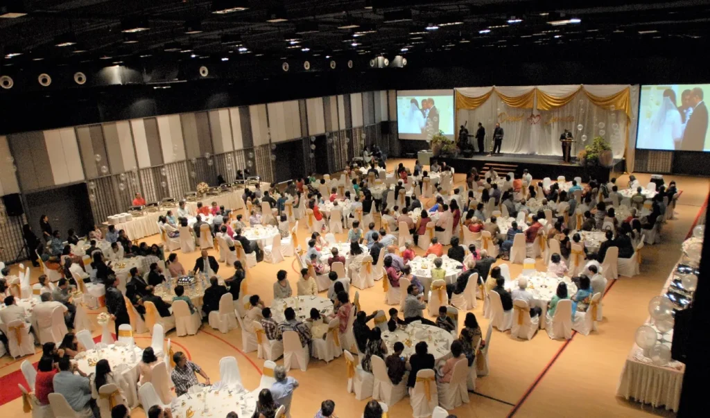 Wedding dinner guests at round tables seen from above, with stage screens, in the Multipurpose Banquet Hall