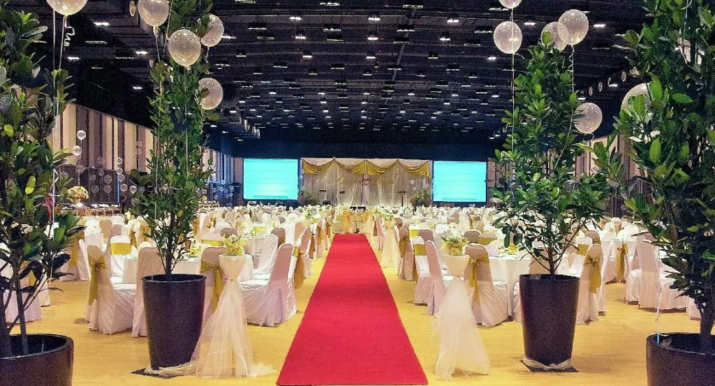 Red carpet aisle between wedding tables and potted trees in the Multipurpose Banquet Hall