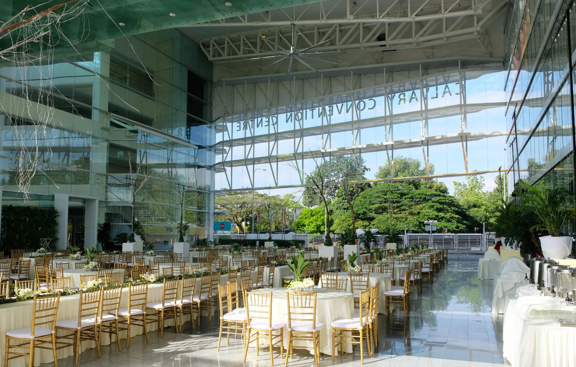 Banquet tables with gold chairs set up in the Plaza under the glass facade