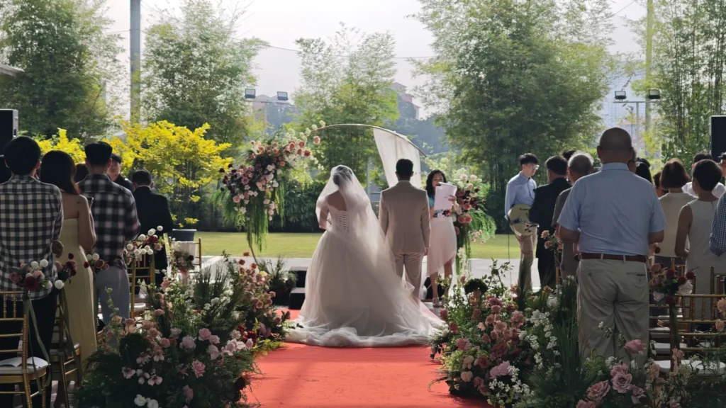Guests standing along a flower-lined aisle as a bride and groom stand at the arch in the Plaza