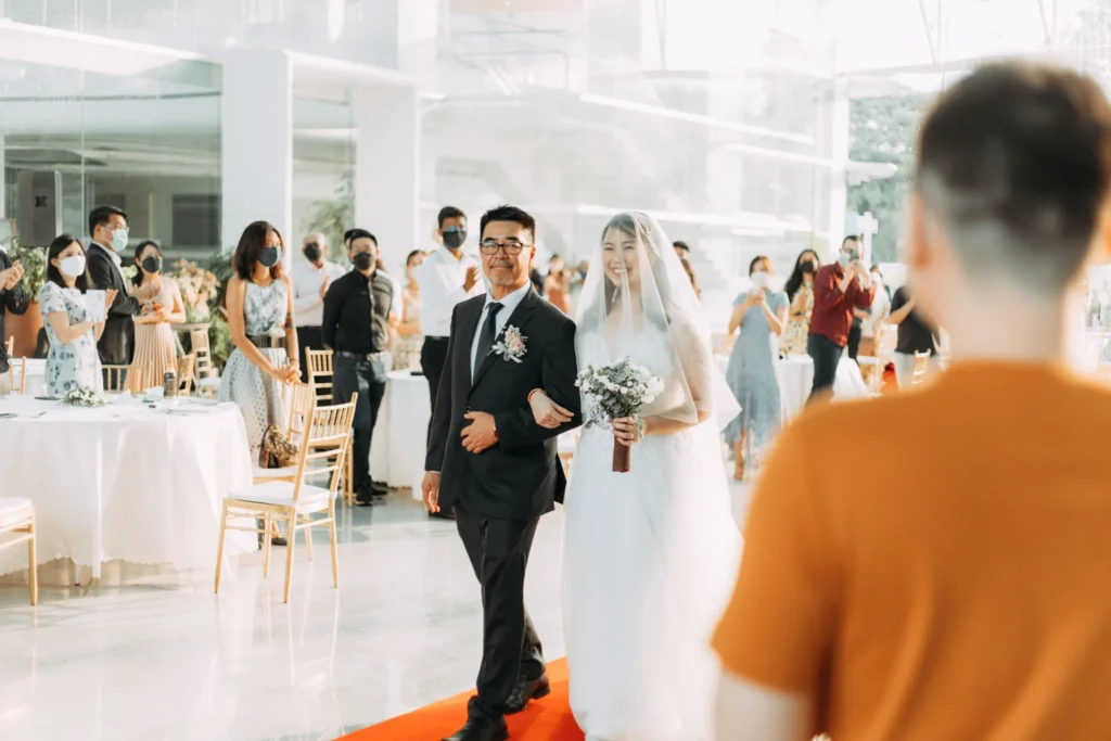 Bride walking in along the red carpet on a man's arm as guests look on in the Plaza