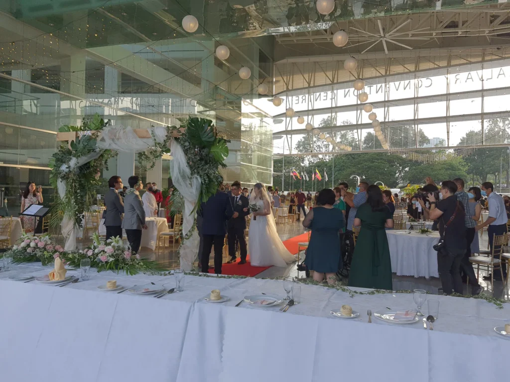 Bride on a man's arm being handed to the groom under a leafy arch as guests watch in the Plaza