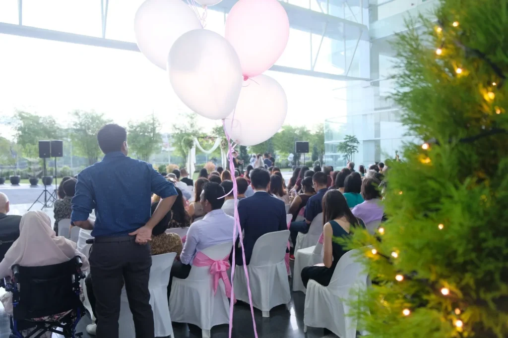 Guests watching a wedding ceremony behind pink balloons in the Plaza