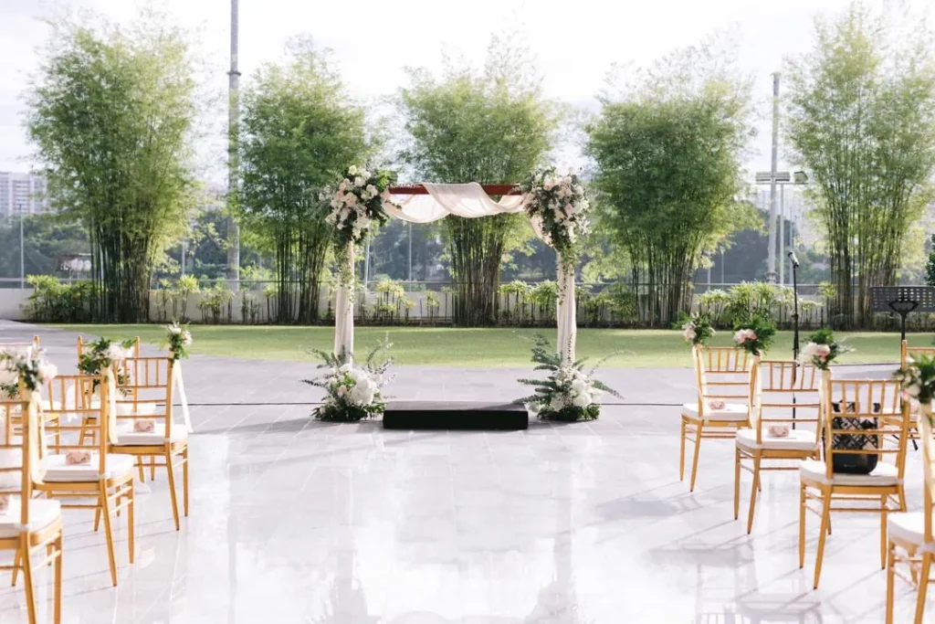 Gold chairs lining an aisle to a flower-draped arch, with bamboo and lawn behind, set up for a Plaza wedding