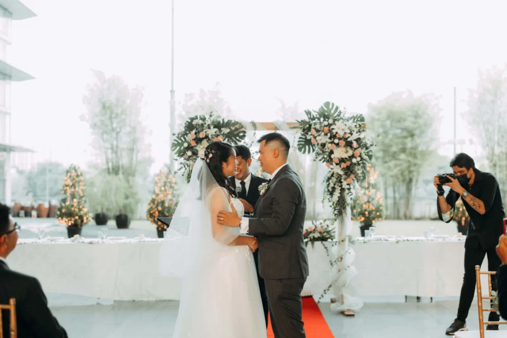 Bride and groom kissing under a floral arch at a wedding in the Plaza