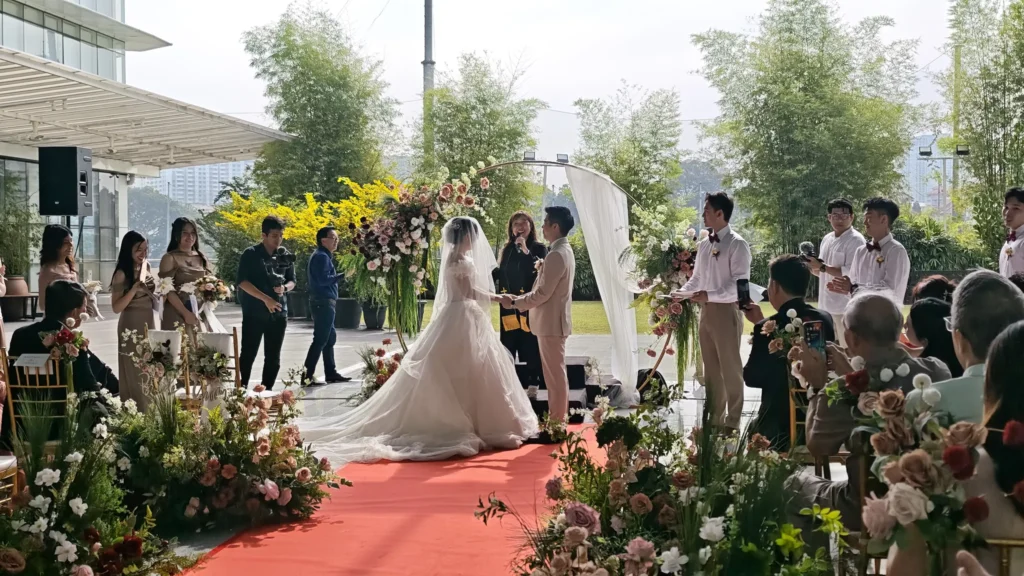 Bride and groom holding hands before an officiant under a floral arch, with bamboo behind, in the Plaza