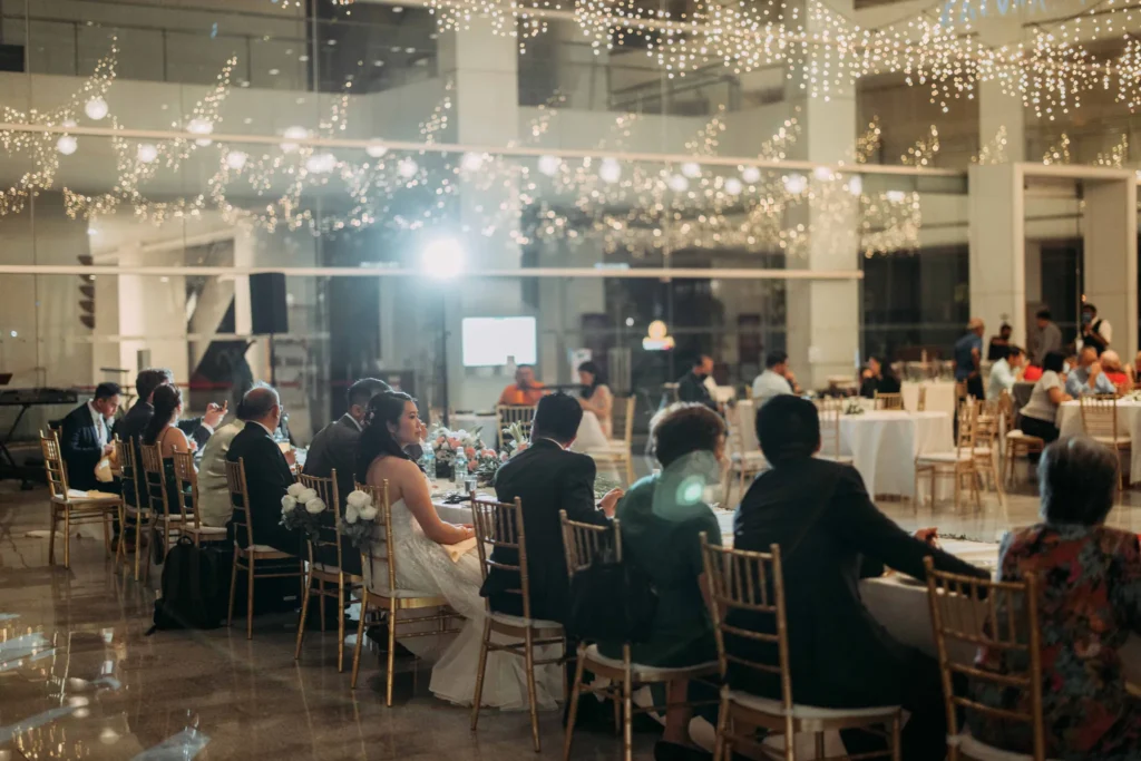 Wedding dinner guests at round tables under fairy lights in the Plaza