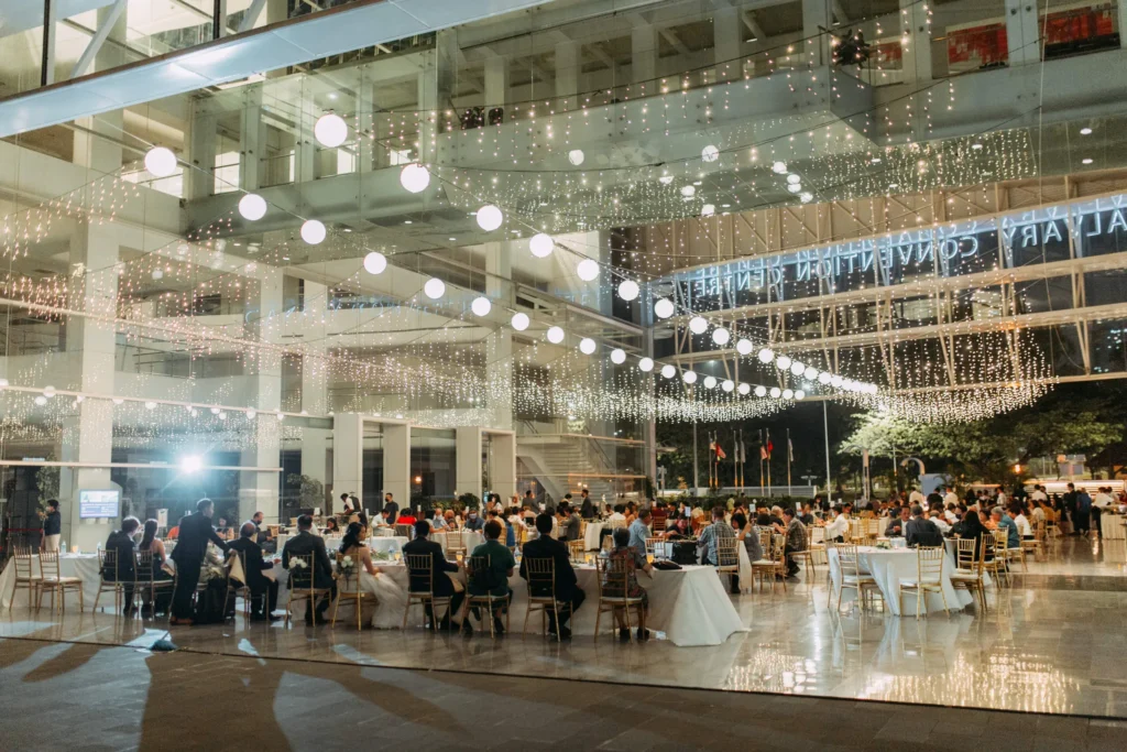Wide view of a wedding dinner under fairy lights in the Plaza at night