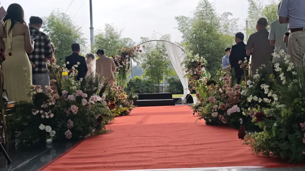 Red carpet aisle lined with pink and white flowers leading to a round arch as guests stand at a Plaza wedding