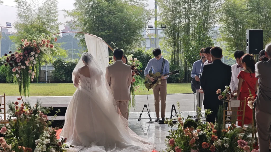 Guitarist playing beside a bride and groom standing at a floral arch in the Plaza