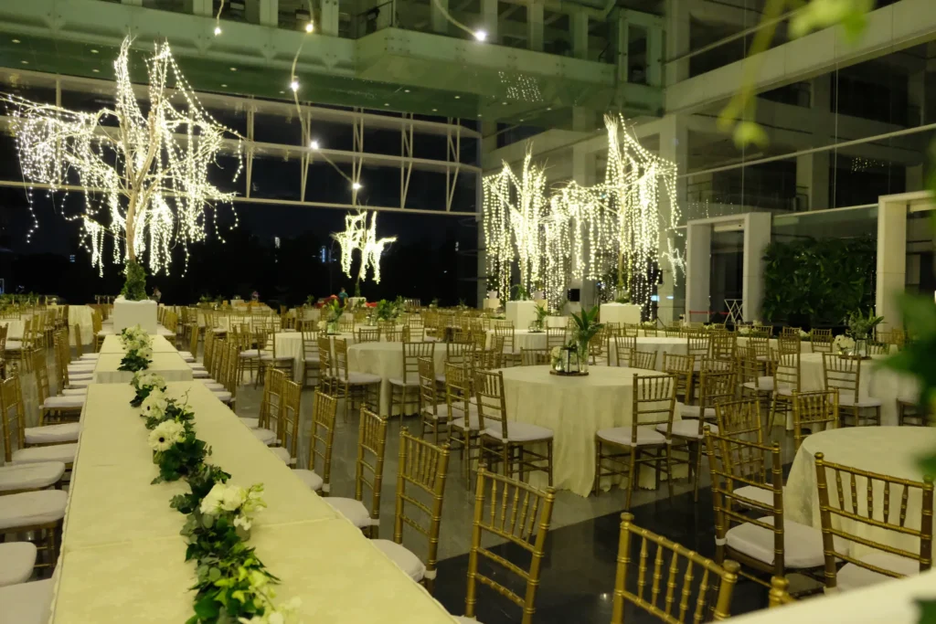 Long table with a white flower garland beside round tables and fairy-lit trees at an evening reception in the Plaza