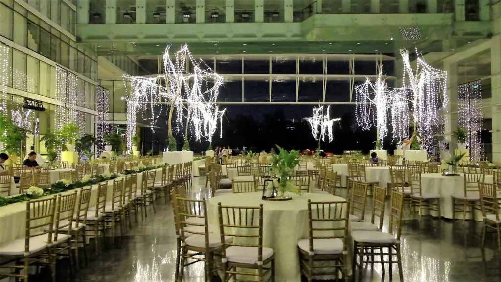 Round tables and gold chairs under trees strung with fairy lights for an evening reception in the Plaza