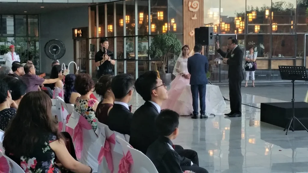 Officiant with a raised hand blessing a bride and groom as guests watch in the Plaza