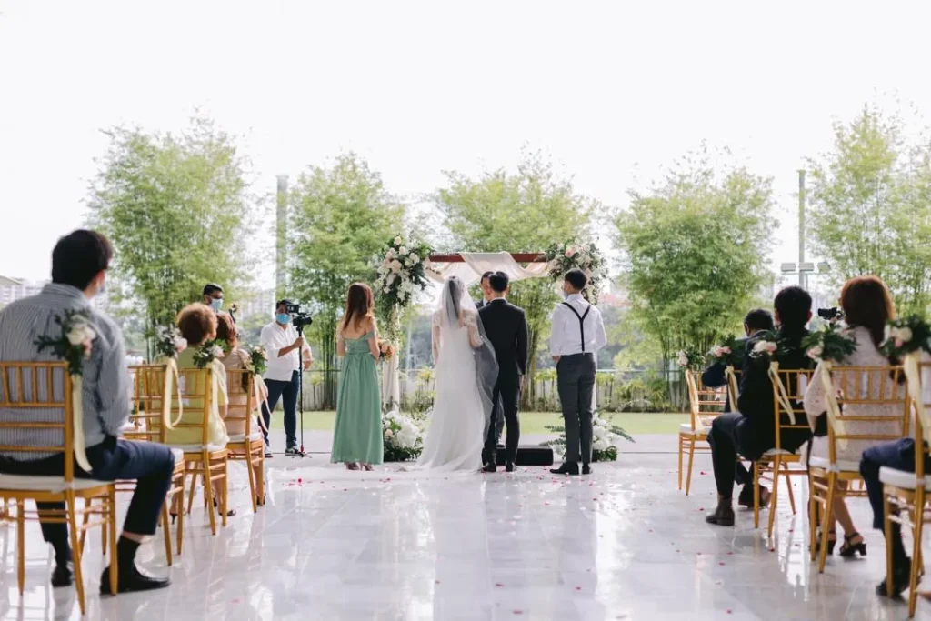 Couple exchanging vows under a floral arch as guests watch in the Plaza