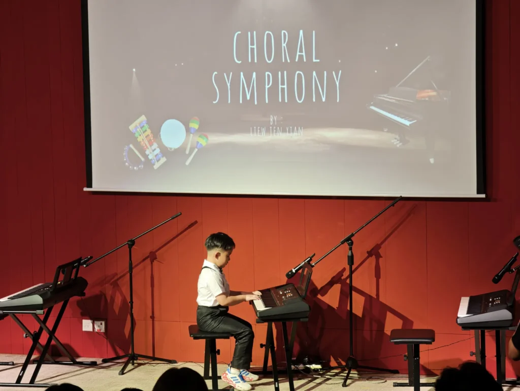 Boy playing a keyboard on a Theatrette stage below a Choral Symphony slide